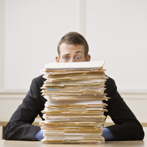 Business man behind tall stack of folders. Square format.