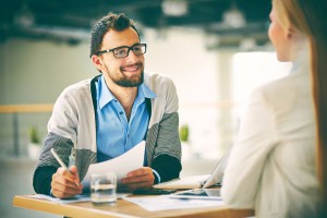 Smiling businessman with paper listening to his colleague at meeting