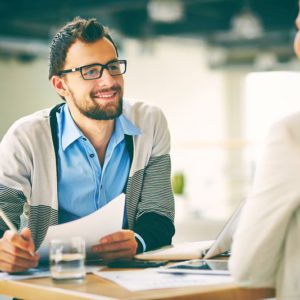 Smiling businessman with paper listening to his colleague at meeting