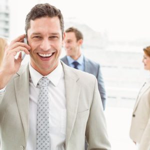 Portrait of businessman using mobile phone with colleagues behind in office