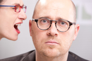 woman shouting in man's ear maybe in a business environment like an office or a meeting room