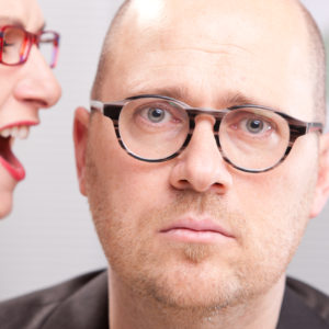 woman shouting in man's ear maybe in a business environment like an office or a meeting room