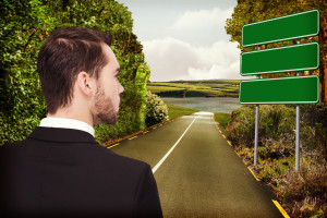 Elegant businessman in suit thinking  against green signs by road