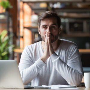 Thoughtful doubtful businessman in tension thinking make difficult decision at work, stressed man put hands in prayer pray with hope pondering reflecting concerned about problem challenge sit at desk