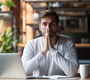 Thoughtful doubtful businessman in tension thinking make difficult decision at work, stressed man put hands in prayer pray with hope pondering reflecting concerned about problem challenge sit at desk