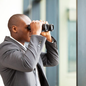 determined african american businessman using binoculars in office