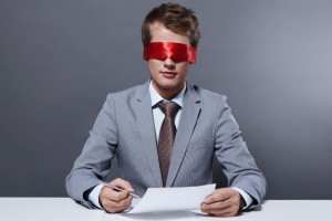 A young businessman signs a contract with a blindfold