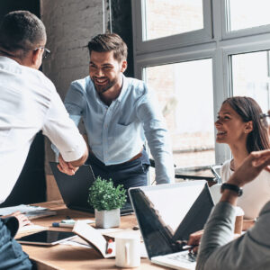 Young modern men in smart casual wear shaking hands and smiling while working in the creative office